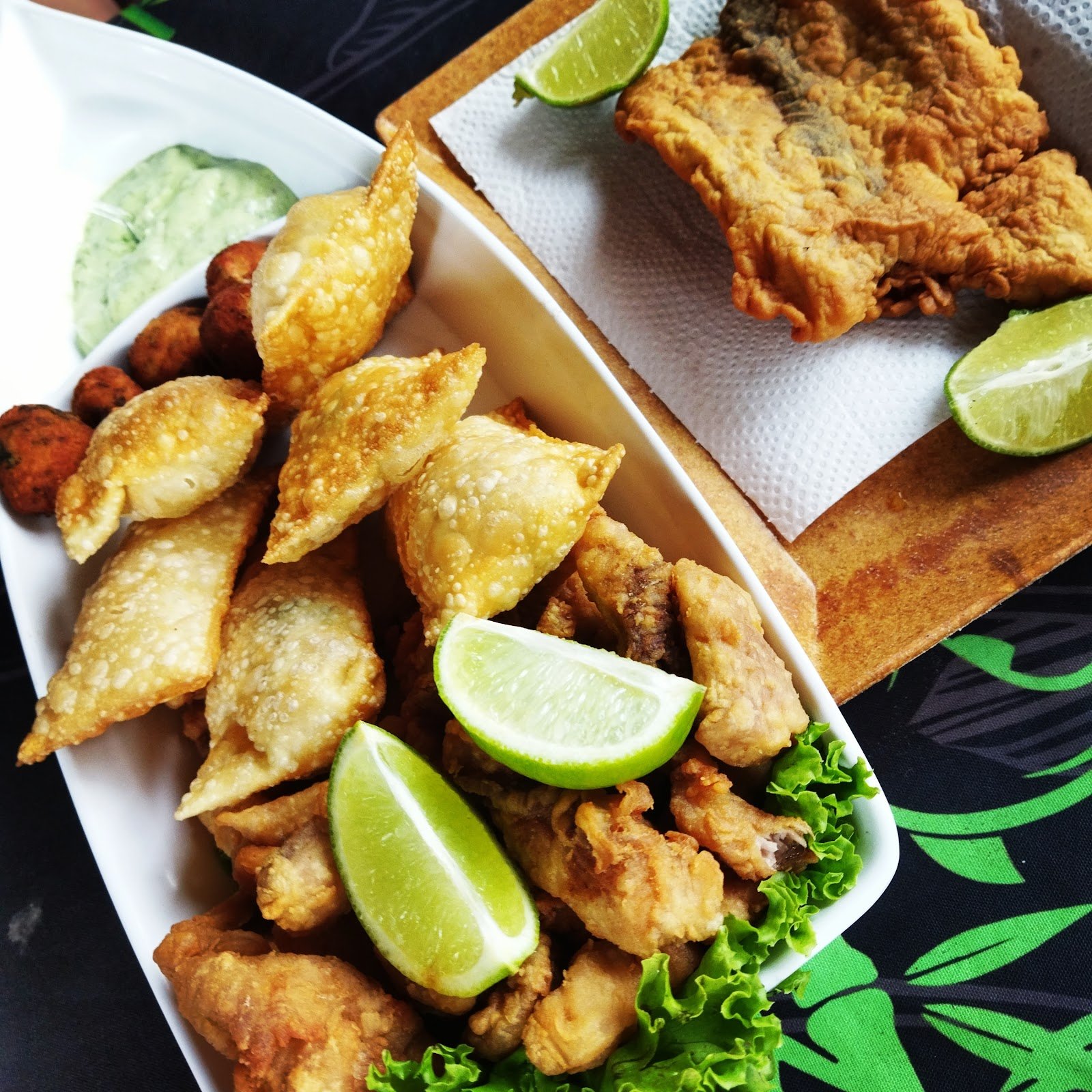 Porções fritas para dividir: pastéis, iscas de peixe crocantes e bolinhos, com limão e molho verde